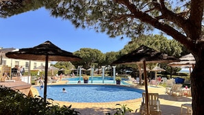 Una piscina amb gandules i ombrel·les, envoltada d'arbres i edificis.