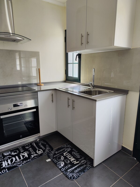 A compact kitchen with a built-in oven, a stainless steel sink, and white cabinetry.