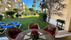 Une terrasse dotée de meubles en osier, une table ornée d’un vase rempli de fleurs rouges et un barbecue.