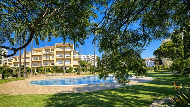Une piscine entourée d’une pelouse bien entretenue, avec un bâtiment doté de balcons en arrière-plan.
