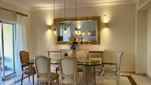 Un espace repas comprenant une table ronde, six chaises, un grand miroir et des luminaires suspendus.
