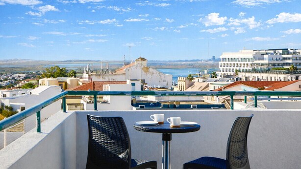 En tagterrasse med udsigt over havet og bygninger, med et bord og stole.