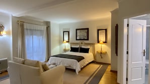 Et hotelværelse med en stor seng, to sengeborde med lamper, en radiator, et vindue med gardiner og en dør.