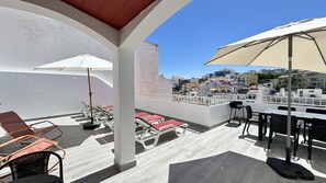 A rooftop terrace with lounge chairs, a table, and umbrellas.