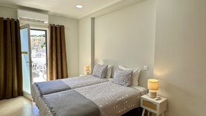 A bedroom with a bed, curtains, a nightstand, a lamp, and a view of the outside.