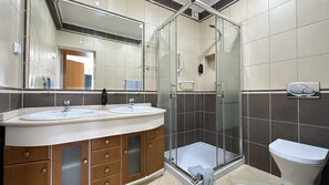 A modern bathroom with two sinks, a glass shower enclosure, and a toilet.