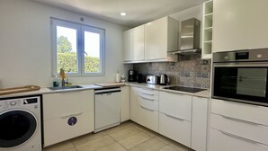 Uma cozinha moderna com armários brancos, máquina de lavar louça embutida, máquina de lavar roupa, cafeteira e forno.