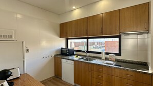 A compact kitchen with wooden cabinets, a microwave, a dishwasher, and a window with a view of a fenced outdoor area. - Medronheira by Check-in Portugal (Albufeira)