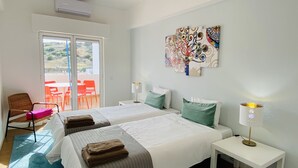 A hotel room with two beds, a balcony with red chairs, and a wall with colorful artwork.