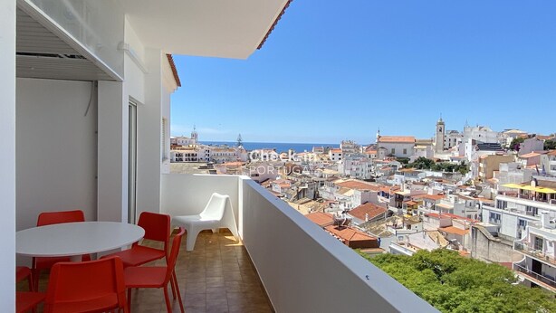 A balcony with a table and chairs, overlooking a cityscape with buildings and a clear sky.