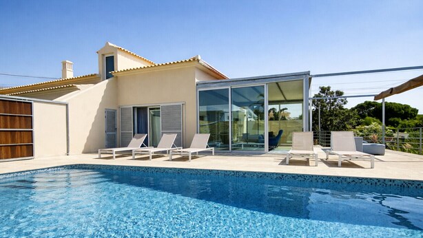 Et moderne hus med swimmingpool, glasdøre og en terrasse med liggestole.