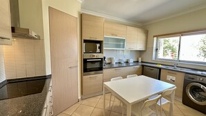 Une cuisine compacte équipée d’un four à micro-ondes, d’un four et d’un lave-vaisselle, une table à manger avec des chaises et une fenêtre donnant sur les arbres.