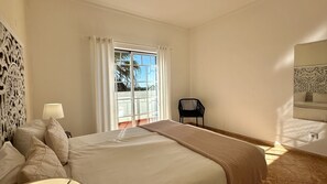 Une chambre à coucher comprenant un lit, une chaise, une lampe, une fenêtre avec des rideaux et un panneau décoratif mural.