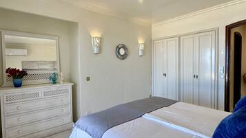 Een slaapkamer met een bed, een dressoir, een spiegel, wandlampen en een deur.