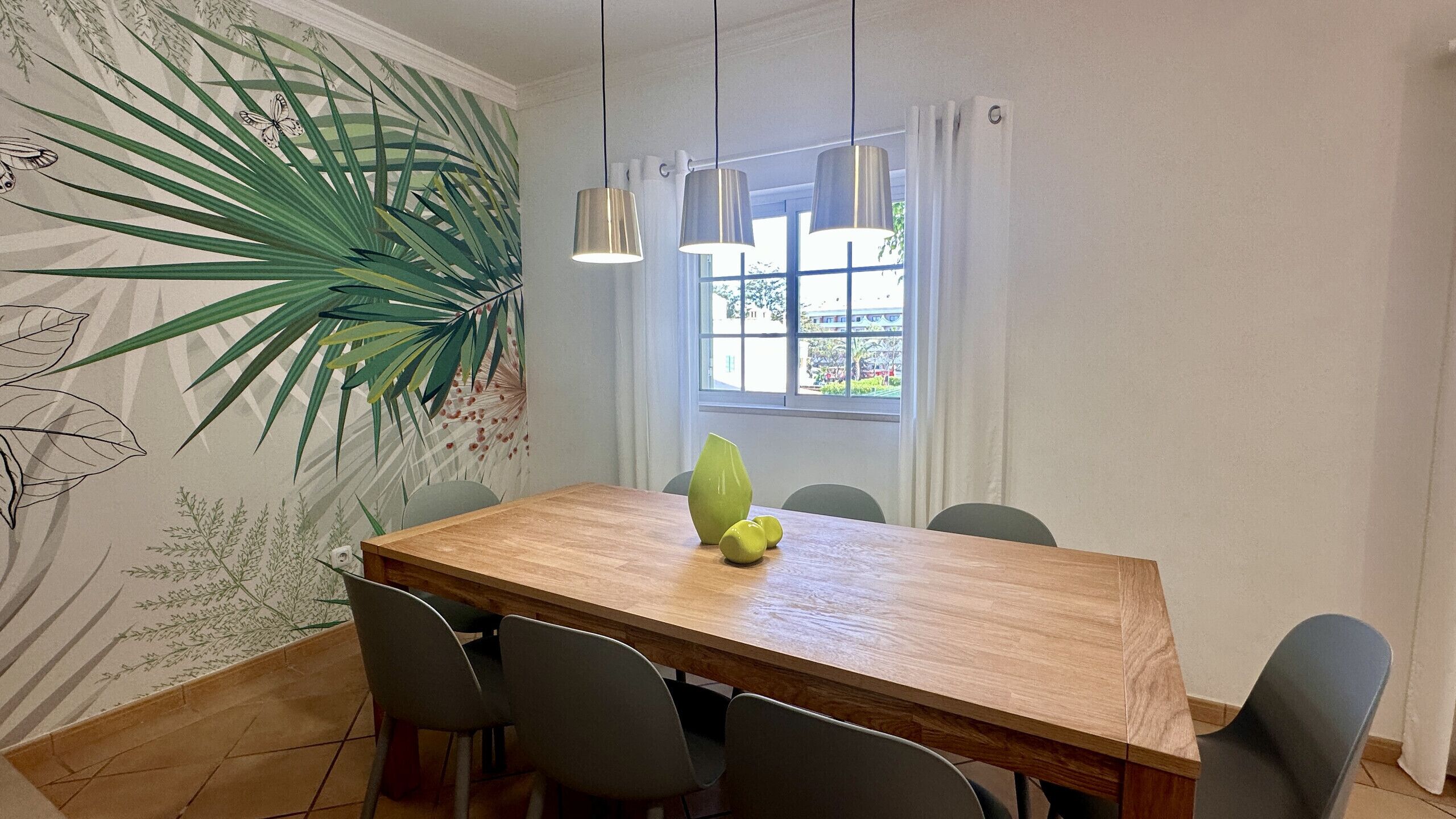 A dining area with a wooden table, six chairs, a green vase, and a large plant.