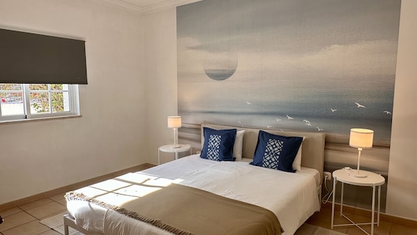 A hotel room with a bed, two bedside tables, a window, and a wall mural.
