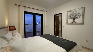 Ein Schlafzimmer mit Bett, Lampe, Blick durch eine Glastür, einem Gemälde und einer Badezimmertür.