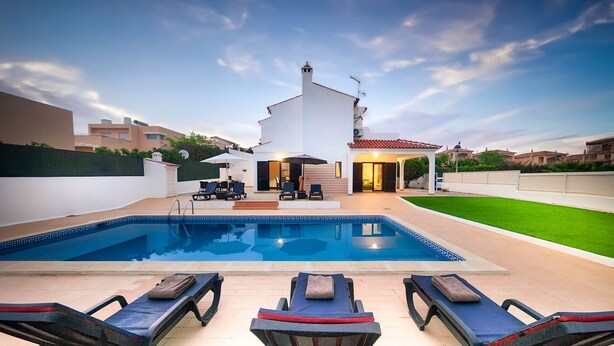 Ein Schwimmbecken mit Liegestühlen, eine überdachte Terrasse und ein Haus mit einem Ziegeldach.