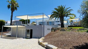 Un edificio moderno con un espacio al aire libre techado, escalones de piedra y palmeras.