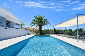 A modern swimming pool with a clear blue mosaic bottom, surrounded by a white building with large windows and a palm tree. - Moderna by Check-in Portugal (Quarteira)