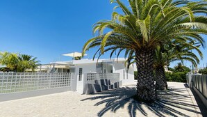 Una casa moderna con fachada blanca, un balcón y una palmera en primer plano.