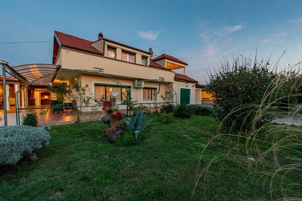 A modern two-story house with a red-tiled roof, a covered patio, and a well-maintained garden.