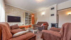Een woonkamer met een flatscreen televisie, bruine banken, een glazen salontafel en een wand met een bakstenen patroon.