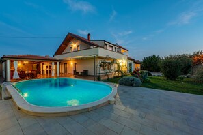A two-story house with a swimming pool, outdoor seating, and a well-maintained garden.