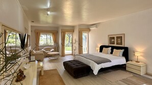Ein Schlafzimmer mit Bett, Nachttischen, einer Kommode, einem Sessel und einem Fenster mit Vorhängen.