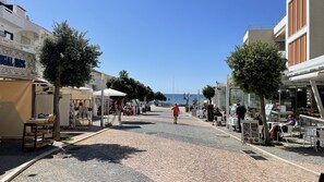 A cobblestone street lined with cafes and shops, a clear blue sky, and a view of the sea in the distance. - Mosqueira by Check-in Portugal (Albufeira)