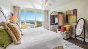 A bedroom with a large bed, a ceiling fan, a TV, a dresser, a chair, and a balcony with a view. - Caribe D814 (Orange Beach)