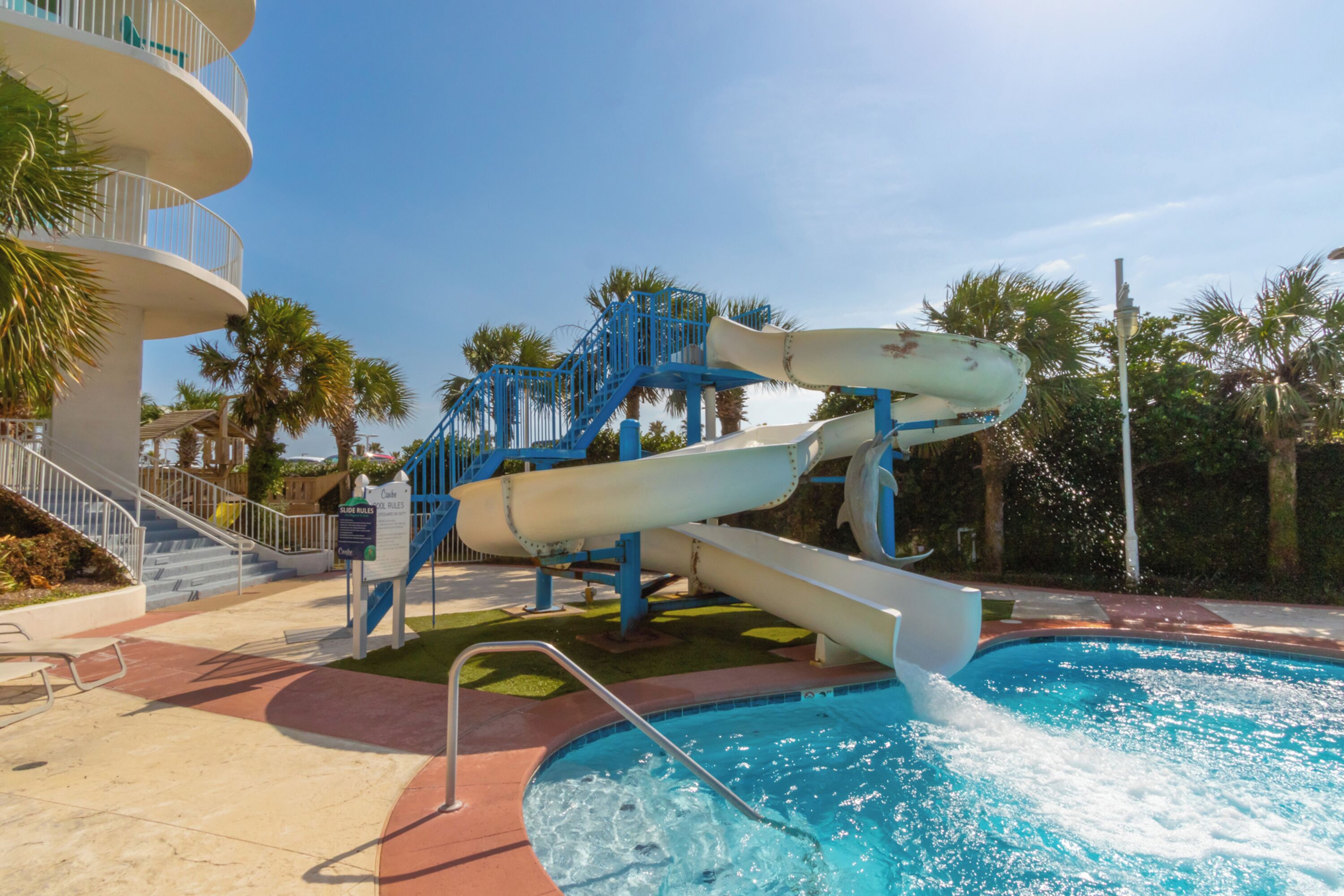 Parque acuático con un tobogán grande, una piscina y una estructura de varios niveles con escaleras.