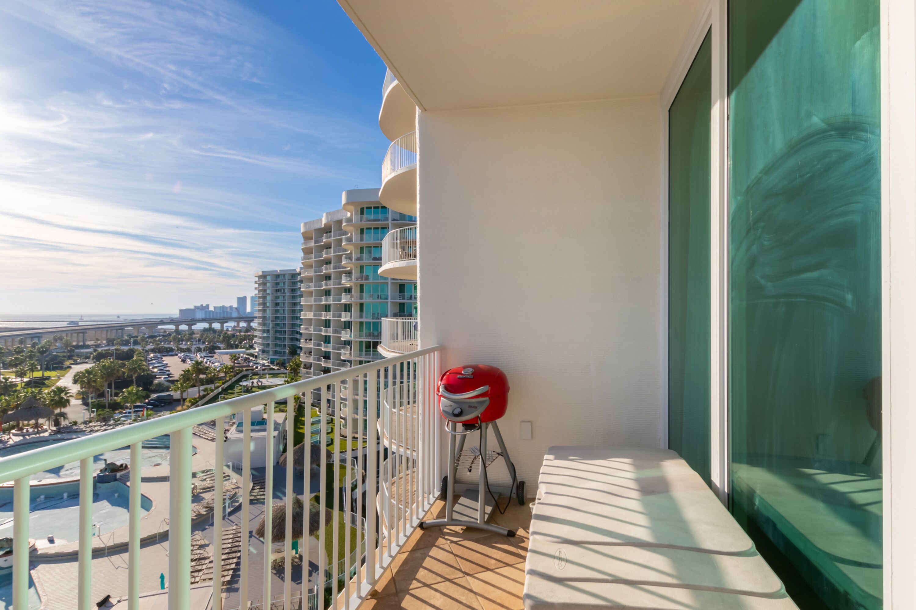 A balcony with a view of a cityscape, a pool, and a red grill.