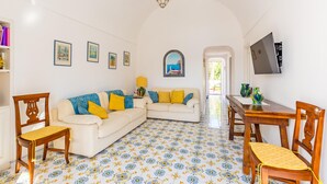 A living room with a white sofa, wooden chairs, a dining table, and a patterned floor. - Capri Turquoise by Napoliapartments (Capri)