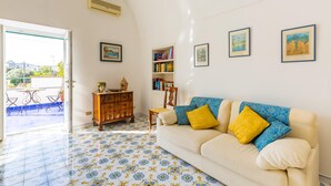 A living room with a white sofa, a wooden cabinet, and a bookshelf. - Capri Turquoise by Napoliapartments (Capri)