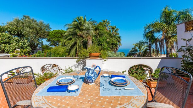 A table set outdoors with a view of the sea, surrounded by chairs and potted plants. - Capri Turquoise by Napoliapartments (Capri)