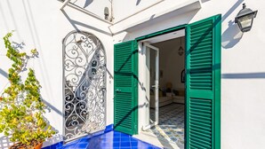 A white building with a blue tiled floor, a decorative metal gate, and green shutters. - Capri Turquoise by Napoliapartments (Capri)