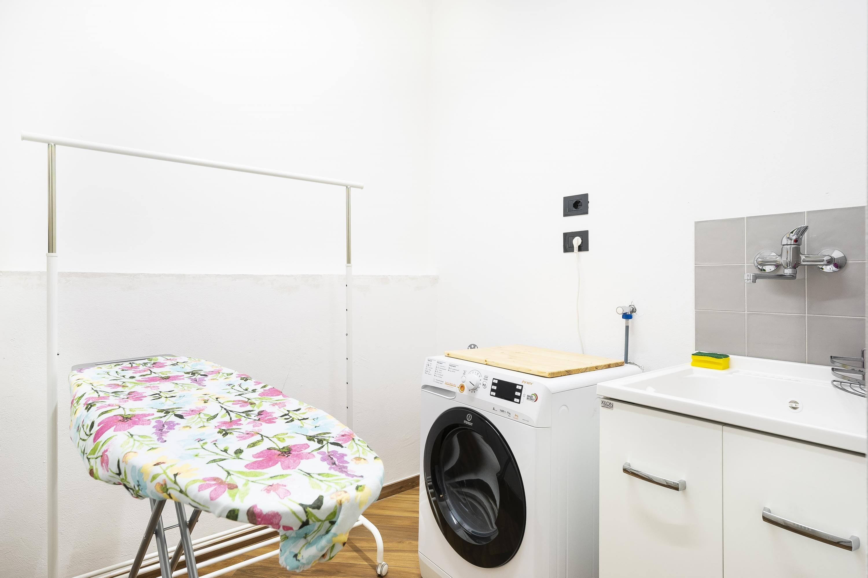 A compact laundry room with a washing machine, a small ironing board, and a sink.