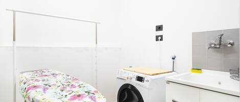 A compact laundry room with a washing machine, a small ironing board, and a sink.