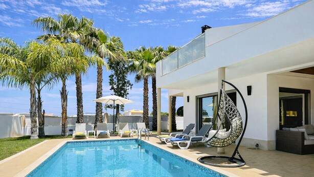 A modern outdoor pool area with lounge chairs, a hanging chair, and palm trees. - Praia by Check-in Portugal (Albufeira)