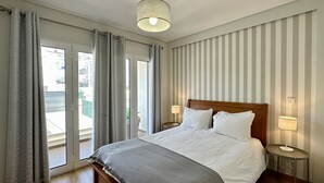 Ein Hotelzimmer mit einem Bett, zwei Nachttischlampen, Blick durch eine Schiebetür und einer gestreiften Wand.