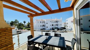 A balcony with a table and chairs, overlooking a white building with balconies.