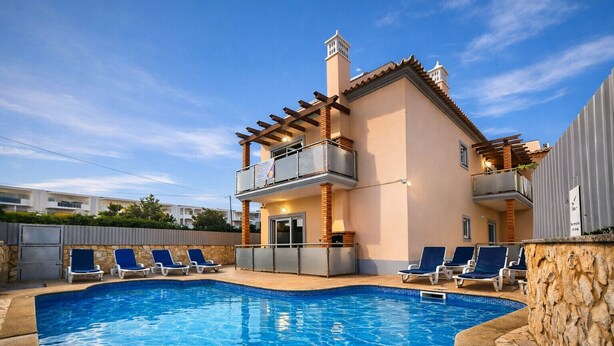 A two-story building with a swimming pool, lounge chairs, and a stone wall.