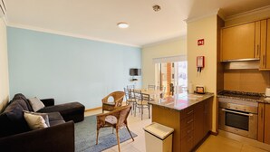 A compact living space with a sofa, a dining area, a kitchen with a stove and cabinets, and a television mounted on the wall.