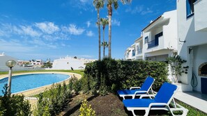 Un espace piscine agrémenté de chaises longues, de palmiers et d’un bâtiment blanc aux touches de bleu.