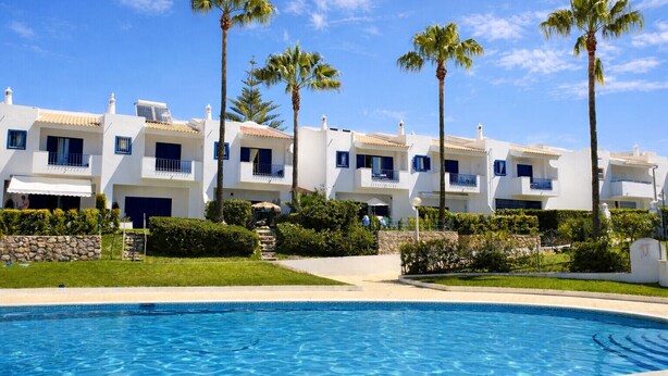 Ett semesterhotell med vita byggnader, balkonger och en swimmingpool.