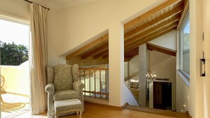 A spacious room with a high ceiling, wooden beams, a large window, and a comfortable armchair. - Azaleas by Check-in Portugal (Vilamoura)