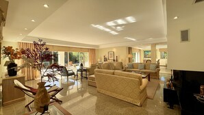 A spacious living room with a large sofa set, a coffee table, and a TV. There is a dining area with chairs and a table, and a decorative plant in the corner. - Azaleas by Check-in Portugal (Vilamoura)