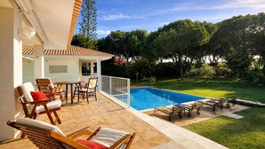 A poolside area with a dining table and chairs, a pool, and a grassy lawn with trees. - Azaleas by Check-in Portugal (Vilamoura)