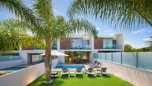 Uma casa moderna de dois andares com piscina, área de estar externa e vegetação exuberante.